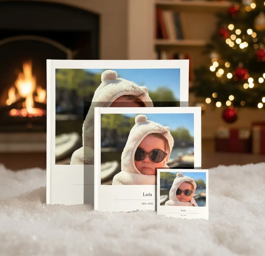 Three sizes of klikkie photo book on snow with a fireplace and lit christmas tree in the background